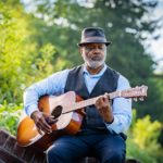 older well-dressed black musician playing acoustic guitar