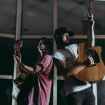 a male - female couple back to back playing acoustic guitars