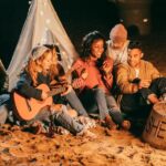 group of young people sitting around a campfire playing music
