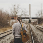 musician with guitar walking along a railtrack