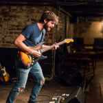young man playing electric guitar in a club
