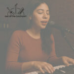 young woman in an open mic in a basement bar playing a piano keyboard and singing gently into a microphone