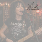 woman in Ramones t-shirt playing guitar and singing at an open mic
