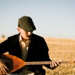 man wearing cap playing a long-necked guitar