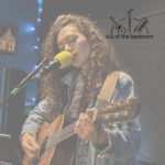 young woman playing guitar and singing at an open mic