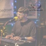 man playing piano and singing into a microphone at an open mic night