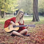 young woman playing guitar sitting in autumn leaves